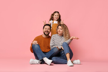 Happy parents and their daughter posing on pink background. Family bonding