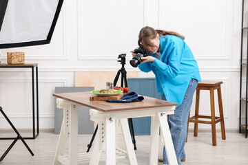 Woman taking picture of salmon with vegetables at table in studio. Professional food photography