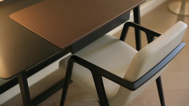 White seat and dark desk sit in quiet space with soft light. Leather pad and clean lines make setup feel calm and modern. Chair and lamp add gentle touch.