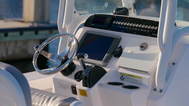 Console of motorboat shows wheel, screen, and buttons. Dock and water are seen behind. Labels give warnings, switches control parts, everything looks ready to use.