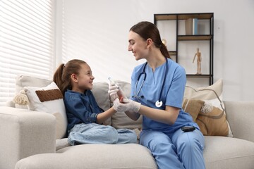 Diabetes. Smiling doctor in medical gloves checking little girl's blood sugar level with lancet pen...