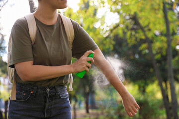 Woman spraying tick repellent onto arm in park, closeup. Space for text