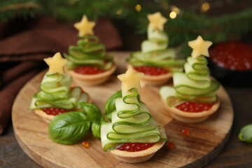 Christmas tree shaped tartlets made with red caviar, cucumber and cheese on wooden table, closeup