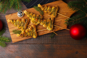 Obraz premium Christmas trees made with puff pastry, pesto sauce, cheese and festive decor on wooden table, flat lay. Space for text