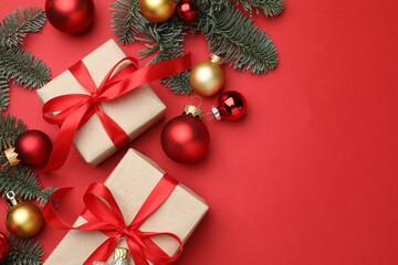 Fir tree branches, gifts and Christmas decor on red background, flat lay. Space for text