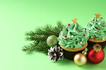 Christmas tree shaped cupcakes and festive decor on green background, closeup. Space for text