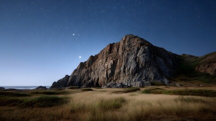 A dramatic coastal landscape at night with a rocky cliff starry sky and windswept grass