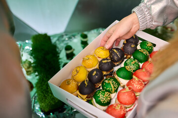 Colorful miniature burger macarons displayed on shiny green foil surface, Playfully arranged rainbow hued miniature burger macarons with glossy shells and festive appeal