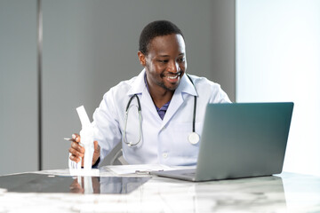 Professional doctor explaining a medical model while working with a laptop during an online consultation, showing healthcare expertise and digital technology in a modern clinic office.