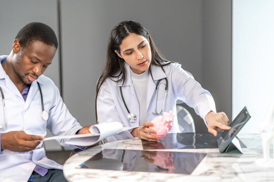 Two professional doctors reviewing a heart model and tablet data together in a modern clinic office, analyzing medical information and discussing patient healthcare using digital technology.
