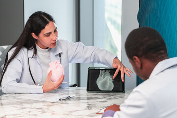 Female doctor showing a heart x-ray on a tablet during a medical meeting in a modern clinic office, explaining healthcare treatment and diagnosis using digital technology and teamwork.