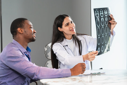 Female doctor showing a brain x-ray result to a patient in a modern clinic office, providing healthcare consultation and professional medical communication for diagnosis and treatment.