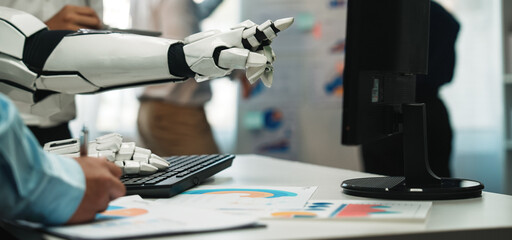A robotic hand pointing at a computer screen, showcasing business charts and data analysis in a...