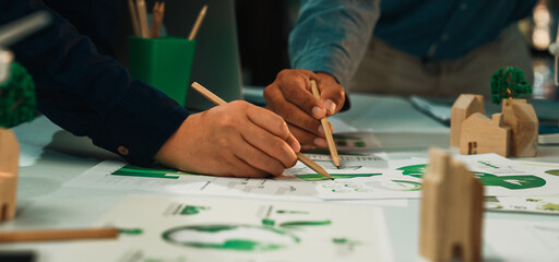 Two individuals collaborate on eco-friendly design sketches in a modern workspace, using pencils...