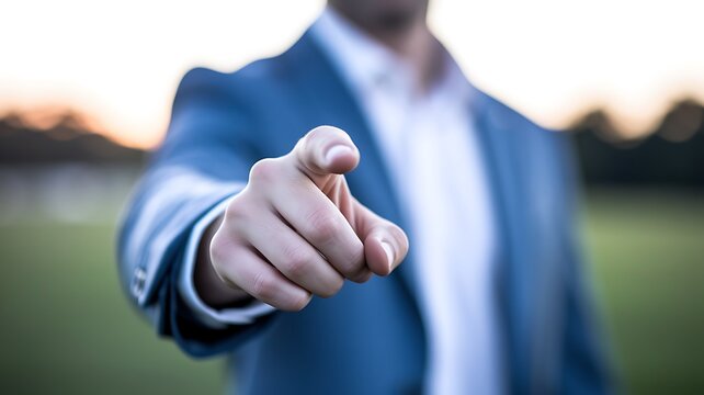 A man in a blue suit points directly at the viewer, symbolizing a call to action, decision, or selection in a professional setting with a blurred outdoor background