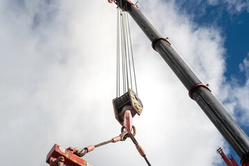 Crane machinery is lifting heavy object using the spreader bar on cloudy sky background. Industrial...