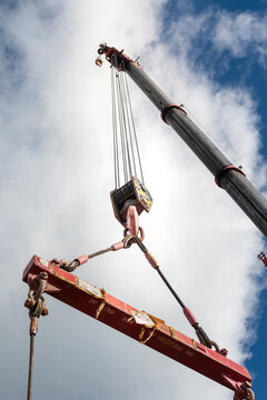 Crane machinery is lifting heavy object using the spreader bar on cloudy sky background. Industrial operation scene and equipment object.