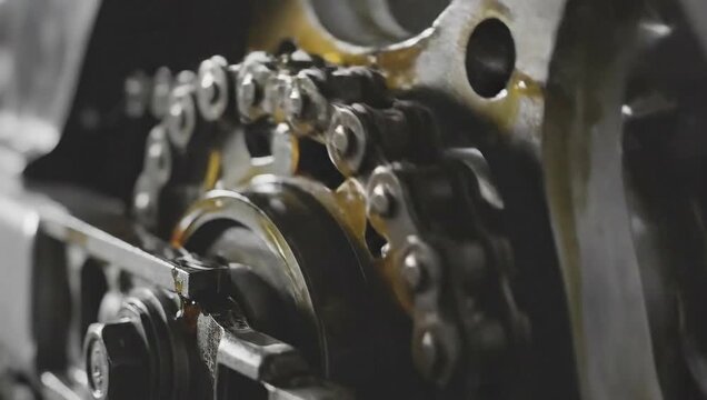 Close up view of a metal chain with oil on a machine in a factory setting with industrial look