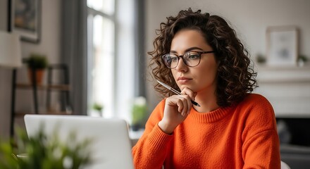Woman with glasses working on a laptop thinking and focused in a home office environment