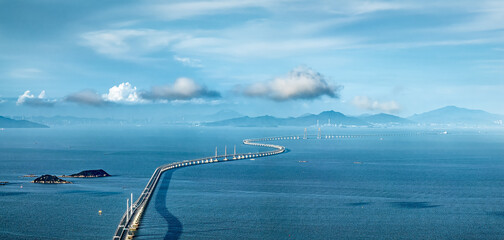 High angle telephoto view of the famous long sea-crossing bridge connecting islands over the blue ocean under a partly cloudy sky.