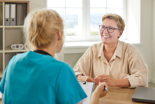 Medical consultation of happy senior woman with doctor in hospital. Smiling patient talking to professional general practitioner, people sitting at desk in clinic for healthcare conversation
