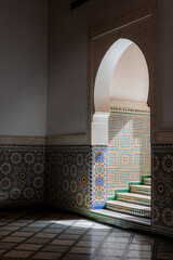 Hard shadows fall across an arched doorway and stairs, highlighting the geometric lines and architectural details inside the Mausoleum of Moulay Ismail in Meknes, Morocco.

