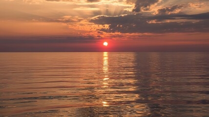 Sunset over calm water reflecting sunlight with cloudy sky above