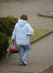 A woman in a blue jacket carries a heavy bag in her hands