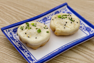 Two sheng jian bao (pan-fried buns) with green onions & sesame, on a blue & white plate. Must-try street food from Bangkok Chinatown night market.
