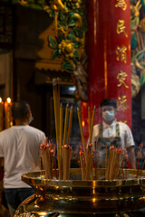 Incense smoke rises from a brass censer in a vibrant Bangkok Chinatown temple, creating a serene worship atmosphere. Glowing embers symbolize devotion.