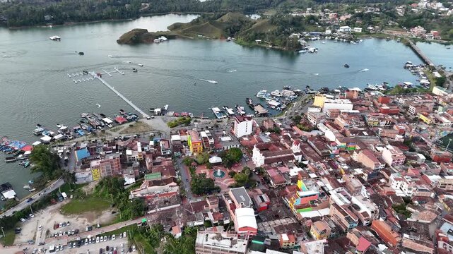 A cinematic aerial shot moves forward and closer to the water's edge in the expansive El Pe&ntilde;ol-Guatap&eacute; Reservoir, showcasing boats, marina, islands, and the town of Guatap&eacute;