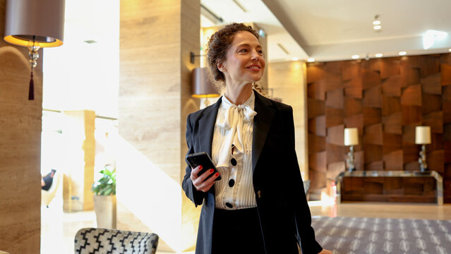 Professional woman arriving or departing from a hotel, holding a phone, embodying business travel, corporate luxury