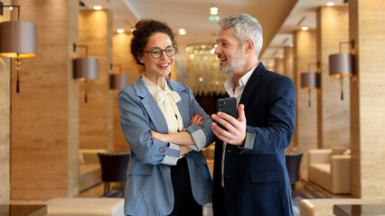 Business colleagues discussing work using smartphone during informal hotel lobby meeting, communicating and networking