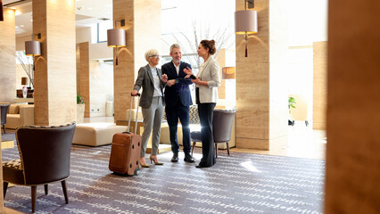 Business couple arriving at hotel, talking with concierge, checking in for corporate travel and hospitality experience