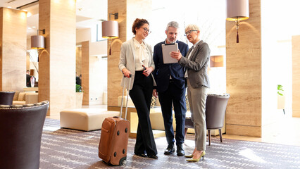 Business colleagues discussing work using tablet computer in a hotel lobby during a corporate travel event