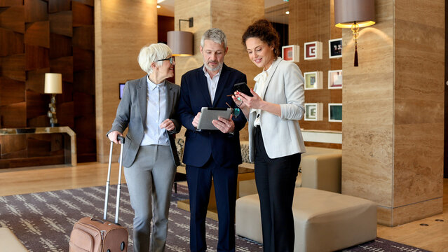 Business professionals having a discussion in hotel lobby using tablet technology and smartphone while traveling