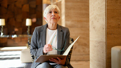 Senior businesswoman holding glasses and file, waiting for an important corporate meeting or job interview