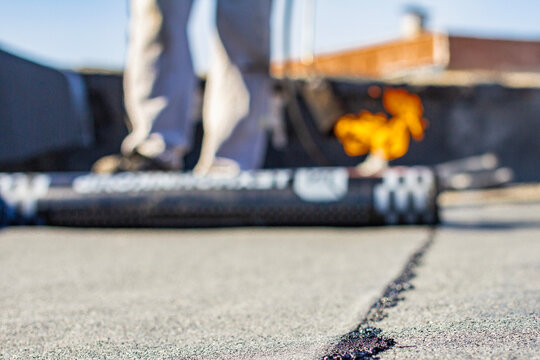 Repairing a soft roof with a fusible material using a gas torch and a propane gas cylinder