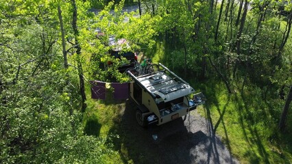 Aerial view of a family camping in a teardrop trailer surrounded by trees, enjoying outdoor activities and quality time together on a sunny day.