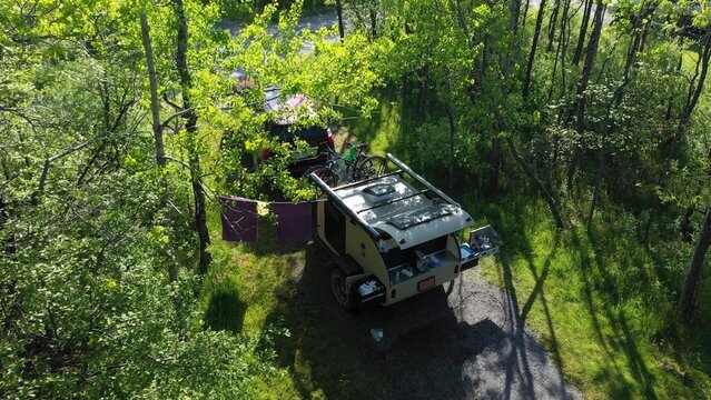 Aerial view of a family camping in a teardrop trailer surrounded by trees, enjoying outdoor activities and quality time together on a sunny day.