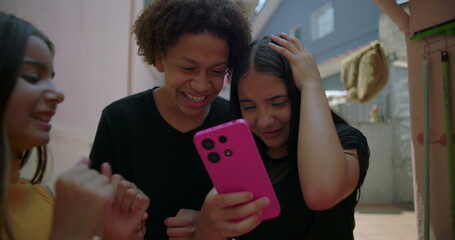 Teenagers reacting to social media post on smartphone in suburban alleyway, one girl showing...