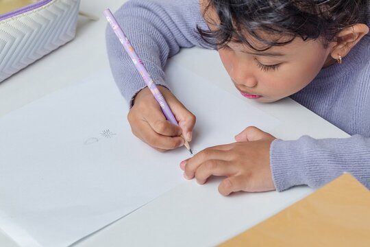 A little Asian girl drawing using a pencil on a table
