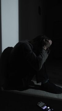 Young man sitting alone in the dark after messaging, feeling ignored and ghosted. Concept of digital heartbreak and loneliness online, vertical video