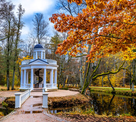 Late autumn in old public park, walking bridge leading to resting pergola

