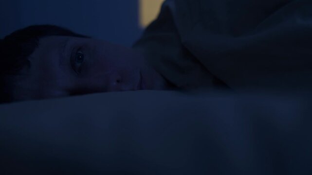 Man suffering from insomnia covering head with blanket at night