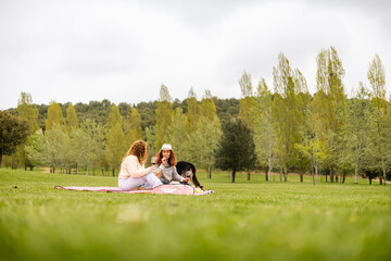 Two women relaxing on a blanket with wine and dog outdoors