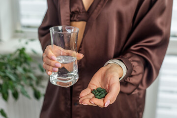Woman holding green supplement pills and water glass