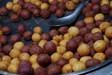 Close-up view of a large, shallow metal tray filled with numerous small, round deep-fried sweet...