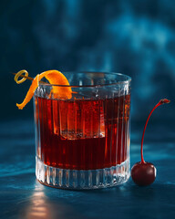 Negroni cocktail in ribbed glass with orange peel garnish and ice, classic red alcoholic drink beverage photography on dark blue background