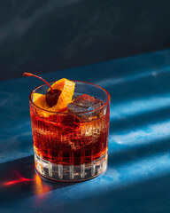 Negroni cocktail in ribbed glass with orange peel and ice on dark blue background, classic red alcoholic drink photography